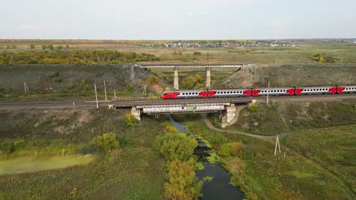 Aerial View of a Railway Bridge with a Passing Passenger Train and the Surrounding Countryside in