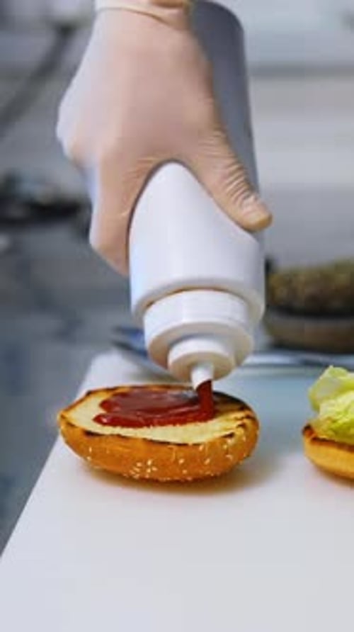 Cook adding ketchup on burger. Preparing burger on kitchen.