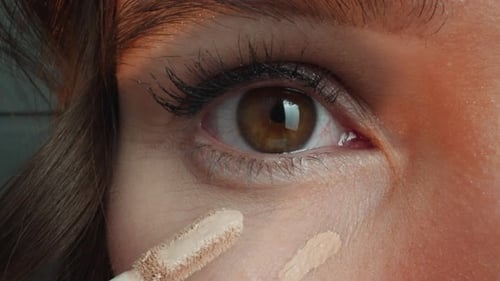 Frau trägt Concealer mit dem Applikator auf die Haut unter den Augen auf