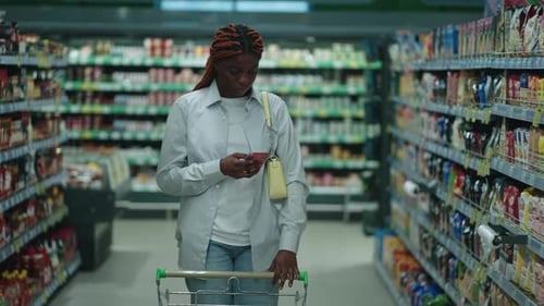 African American Woman Shopping for Fresh Produce in a Supermarket Using Her Digital Gadget to Help