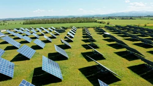 Solar panels in a vast green field under a clear blue sky