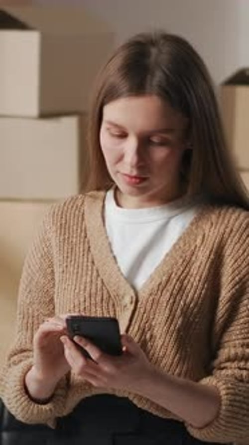 Woman Using Smartphone near Cardboard Boxes Indoors