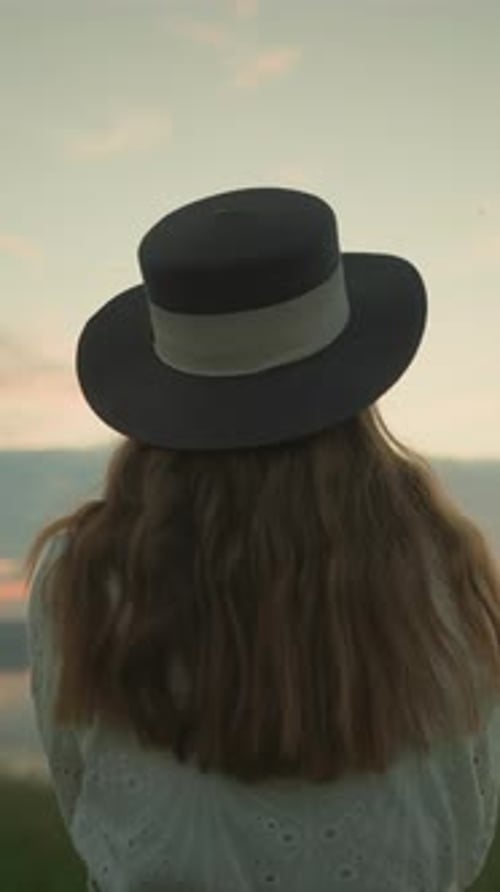 CloseUp of Woman in Hat and White Dress Gazing at Lake During Peaceful Sunset
