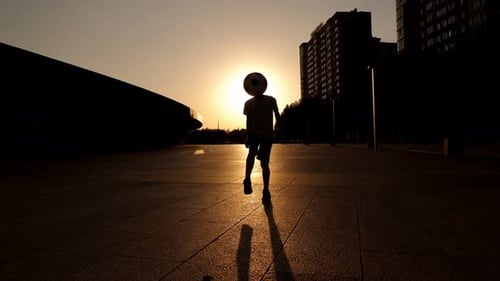 Silhouette of a Little Boy Stuffing a Ball in a City Park in Summer at Sunset