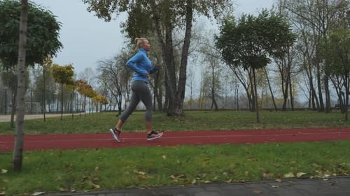 Blonde Woman Jogging at Track in Autumn Morning