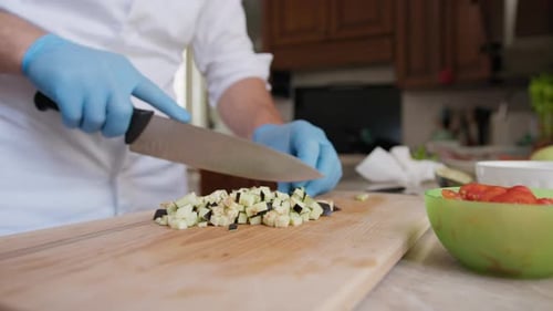 Der Koch schneidet Auberginenfutter auf einem Holzschneidebrett in Brunoise