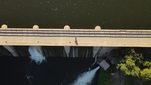 Aerial top down shot of two people walking over bridge and dam dike during sunny day