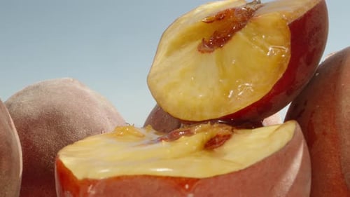 a peach cut in half, water flows through it, peaches under the sun and blue sky, close-up, slow moti