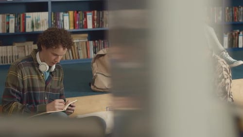 Young College Students Writing Essays in Library and Chatting