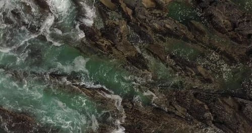 Drone footage of ocean waves washing over rocks.