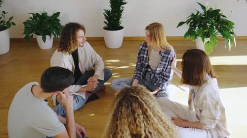 Un groupe de jeunes discute paisiblement sur un plancher en bois entouré de plantes faisant la promotion