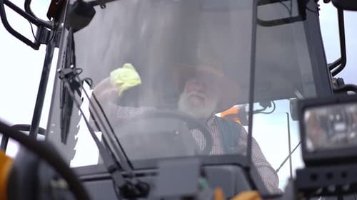 Gray-Bearded Farmer Cleans Tractor Window with Cloth