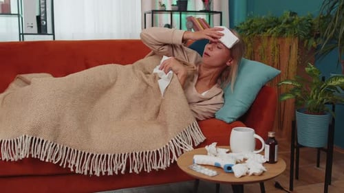 Une femme malade souffrant d'un rhume ou d'une allergie allongée sur le canapé de la maison éternue et essuie la morve dans la serviette