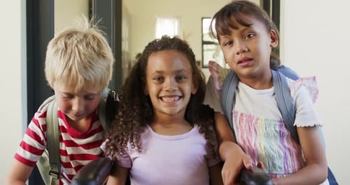 Diverse school-age children posing for camera in entry, leaning toward wheelchair with backpacks