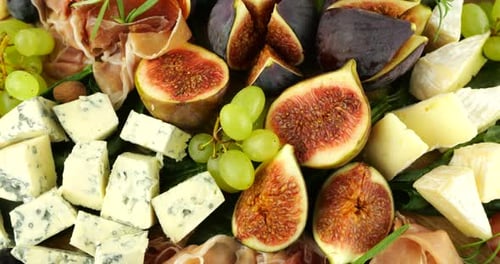 Figues, jamon, feuilles d'épinard, raisins, noix et fromages bleus sur une planche de bois. Set de snacks.