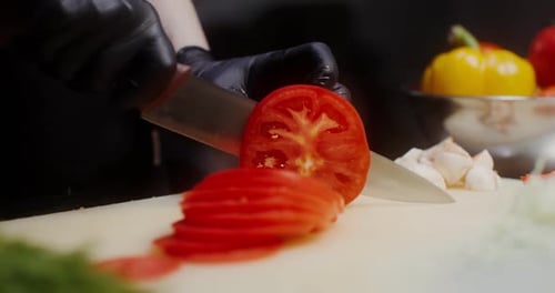 Slicing a tomato with a knife. Close up, hand of unrecognizable male chef cutting tomato