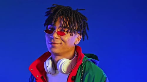 Stilvoller junger afroamerikanischer Mann mit Dreadlocks, lächelt auf blauem, trendigem Outfit