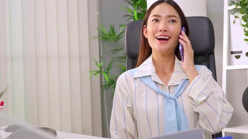 Asian young businesswoman talking on smartphone and working in office.