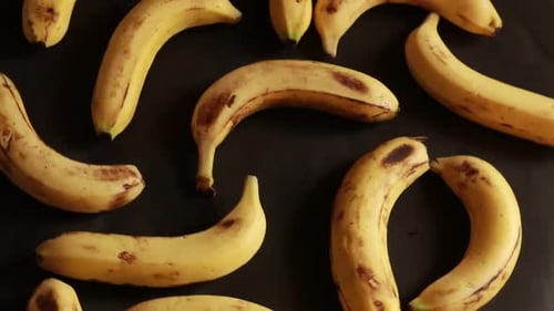 Ripe delicious wet bananas rotate clockwise on a black plate on a black background