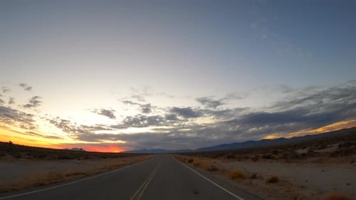Driving along a Mojave Desert road towards the mountains and sunset - driver point of view