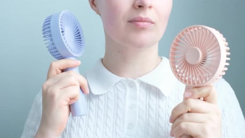 Young woman holding two mini fans on a gray background close-up, front view.
