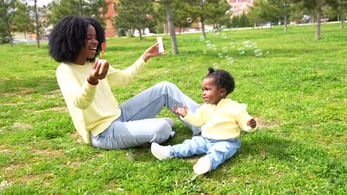 African Mother and Girl on the Park Making Soap Bubbles