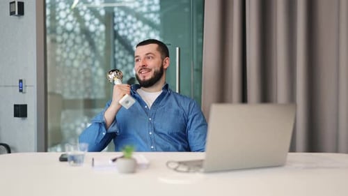 Excited Man Holding Trophy At Desk With Laptop