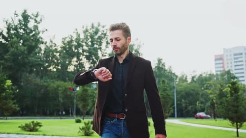 Man Checking Watch While Walking Through a City Park in the Afternoon