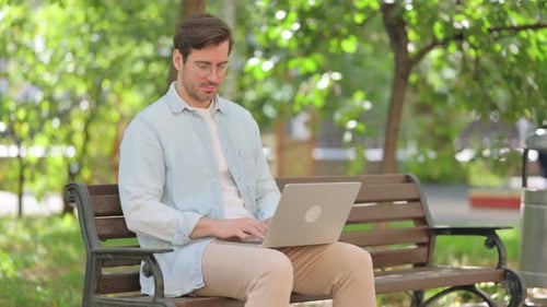 Casual Young Man Using Laptop while Sitting in Park