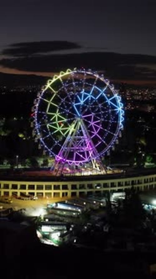 Portrait drone shot toward the illuminated ferris wheel at Aztlan Park, CMDX
