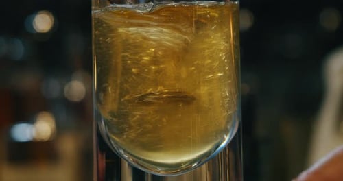 Close up of a professional bartender is preparing an alcoholic cocktail with ice cubes to customer