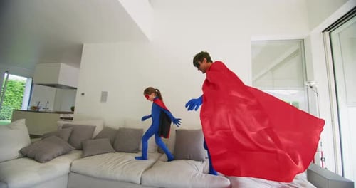 A carefree happy smiling father and daughter dressed as superheroes are having fun to run and jump