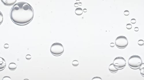 Auf einer transparenten Oberfläche auf weißem Hintergrund bilden sich klare Blasen und schweben zu anderen. Das Medikament