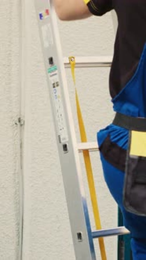 Construction Worker in Blue Coveralls Climbing Ladder