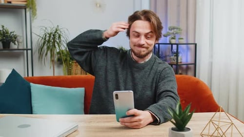 Man Smiling Using Phone at Desk in Living Room
