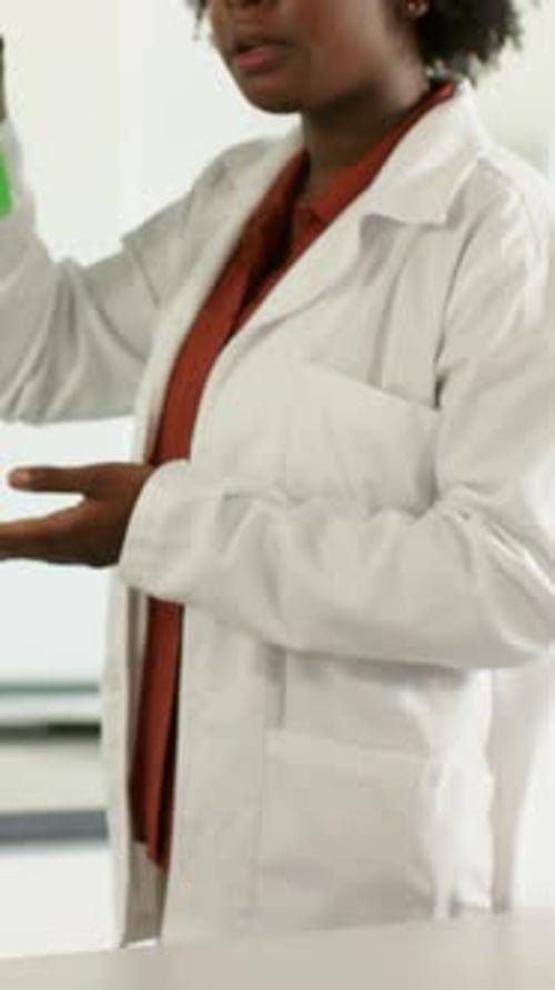 Vidéo verticale : Atteindre un technicien en blouse de laboratoire en blouse de laboratoire en train de vérifier le mélange vert dans un erlenmeyer muni d'une tige