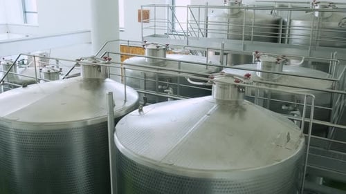 Blick von oben auf große Fermentationstanks in einer Weinkellerei, die mit Metallplattformen und Rohren verbunden sind