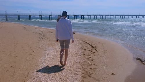Woman Traveller Walks on Shells Sea Water and Sand on the Beach Wearing in Hat