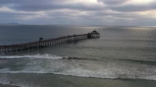 Surfers Swimming At Imperial Beach Pier In San Diego On A Cloudy Sunset. drone forward descend