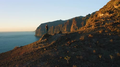 Man Backpacker Standing on Mountain Top with Ocean View at Sunset