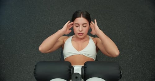 Ansicht von oben auf ein Mädchen in einer weißen Sportuniform, das Situps macht und ihre Bauchmuskeln auf einem