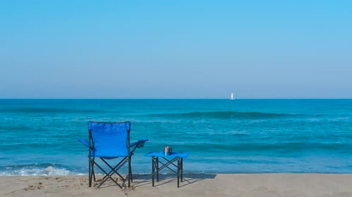Leerer blauer Strandstuhl und kleiner Tisch mit Blick auf ruhige Meereswellen