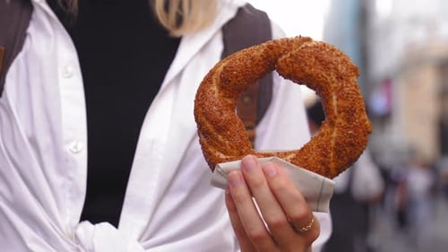 Girl tourist holding simit close-up on city street on sunny day without face.