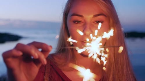 Face, sparkler and new year with a woman on the beach at night for a celebration event
