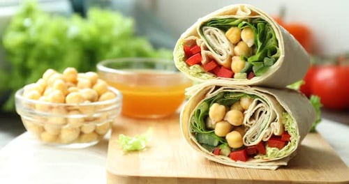 Brett mit leckeren Wrap-Stücken mit Kichererbsen, Sauce und Gemüse vor dem Hintergrund