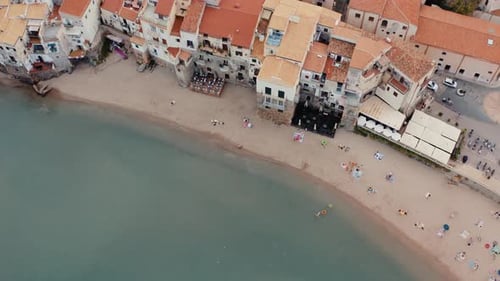 Aerial top down view to a beach in Cefalu. Buildings near water. Clay tiled roofs from above. Town i