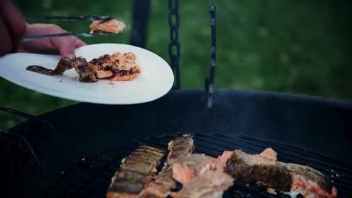 Taking a piece of a red fish with tongs from the barbecue grill