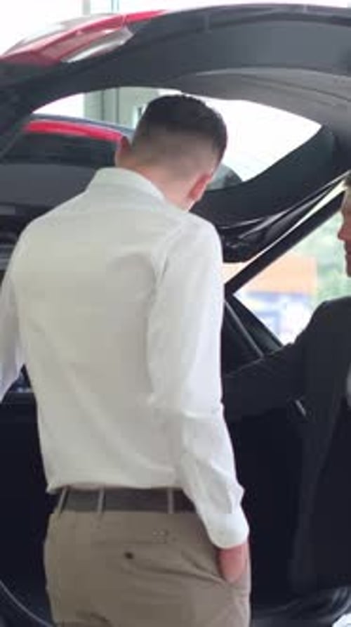 A Salesman at a Car Dealership Shows a New SUV to a Customer Vertical Video