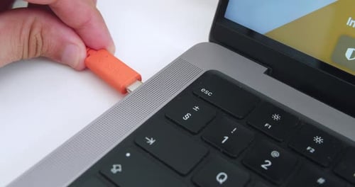 Amazing slow motion close up shot of young man's hand plugging orange lacie disk usb c cable into pr