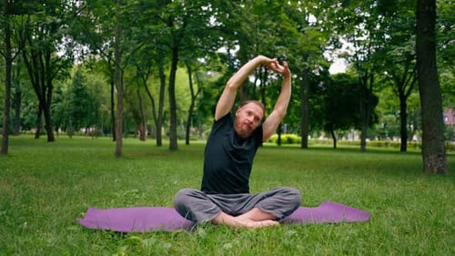handsome bearded man meditating in the park practicing yoga doing stretching and exercises